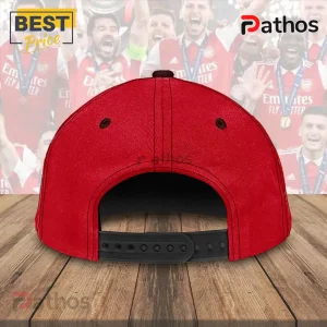 Arsenal FC The Gunners Premier League Champions 25/26 Classic Cap 3 Bright red baseball cap with black snapback closure on wooden surface with blurred sports team background!