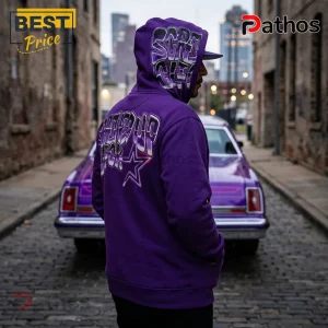 Man wearing purple hoodie with rhinestone text SCARFACE and star graphic, standing before a purple lowrider car in alley.!