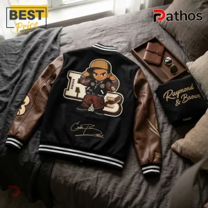 Black wool and brown leather varsity jacket with cartoon character graphic, initials RB, and script embroidery on bed.!