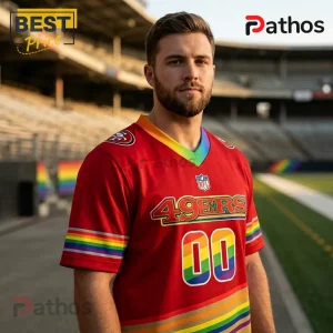 San Francisco 49ers x LGBTQ Pride Limited Edition Football Jersey 2 Man wearing red San Francisco 49ers jersey with rainbow pride stripes on collar, sleeves, numbers, and hem at stadium.!