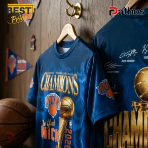 New York Knicks 2026 champions graphic t-shirt in blue with gold text and Larry O'Brien trophy print on wood wall.!