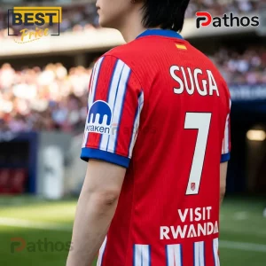 Person wearing a red soccer jersey with white and blue striped sleeves, number 7, SUGA, and VISIT RWANDA text on back.!