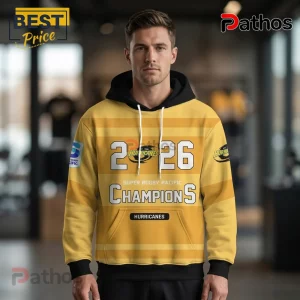 Yellow and black Hurricanes Super Rugby Pacific 2026 champions hoodie worn by a man against a blurred shop interior.!