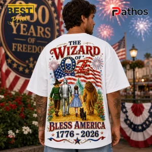 The Wizard of Oz Bless America 1776-2026 Patriotic T-Shirt 4 White oversized t-shirt featuring The Wizard of Oz characters walking on yellow brick road under American flag and fireworks.!