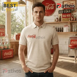 Man wearing a beige gingham polo shirt with a red Coca-Cola logo inside a vintage-style soda fountain diner setting.!