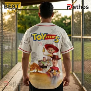 Toy Story 5 baseball jersey featuring Woody, Buzz Lightyear, and Jessie on a beige fabric with red trim and graphics.!
