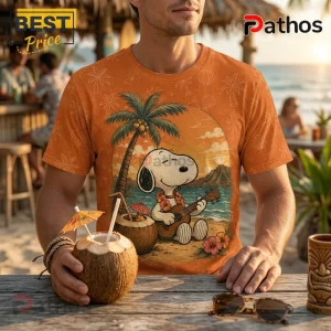 Orange graphic t-shirt featuring Snoopy playing a ukulele on a beach with a palm tree, coconut, and hibiscus flowers.!