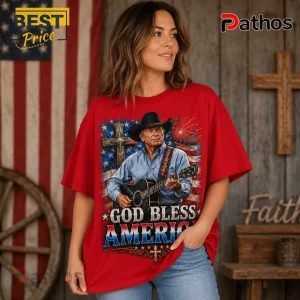 Woman wearing a red t-shirt with a cowboy playing guitar, a cross, and American flag graphic reading God Bless America.!