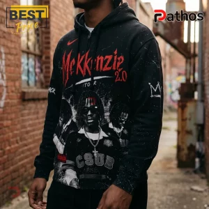 Black zip-up hoodie featuring red McKkenzie 2.0 text and rap-inspired graphic prints worn in an urban brick alleyway.!