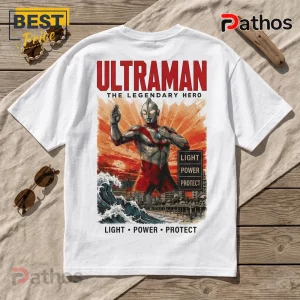 White cotton t-shirt featuring graphic art of Ultraman standing over a cityscape with ocean waves, red sunset, and text.!