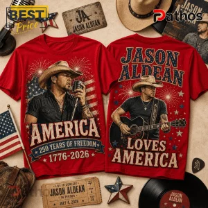 Jason Aldean America 250 Years 1776-2026 Patriotic Concert T-Shirt 1 Two red cotton t-shirts with Jason Aldean prints, American flag motifs, fireworks, and patriotic text on a wooden surface.!