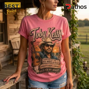 Pink t-shirt with Toby Keith graphic, cowboy hat illustration, acoustic guitar, and country song lyrics on a wooden porch.!