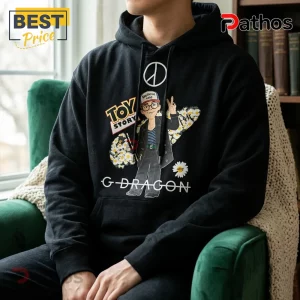 G-Dragon x Toy Story Bullseye Daisy Black Hoodie 1 Black cotton hoodie featuring G-Dragon cartoon graphic, Toy Story logo, white daisy floral print, and peace sign symbol.!