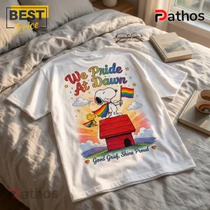Snoopy Pride Rainbow LGBTQ T-Shirt 2026 1 White cotton t-shirt featuring Snoopy and Woodstock with a rainbow flag on a doghouse. Text reads We Pride At Dawn.!