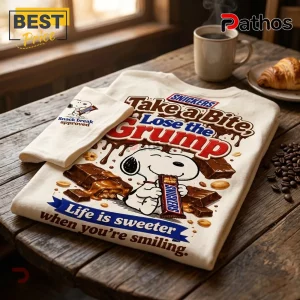 Snoopy x Snickers Snack Break T-Shirt 1 Cream-colored t-shirt featuring Snoopy holding a Snickers bar with text reading Take a Bite, Lose the Grump.!