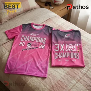 Two pink and grey Adelaide Thunderbirds netball champion jerseys featuring team logos and text on a beige bedspread.!