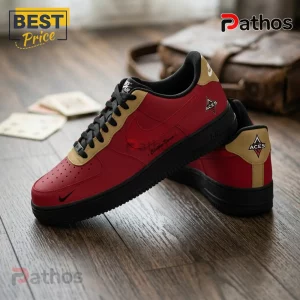 Custom red, black, and gold leather sneaker with Aces logo on the heel and side, resting on a wooden floor.!