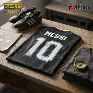 Messi x Spider-Man Argentina Black Football Jersey 1 Black soccer jersey with blue spiderweb pattern, Messi name and number 10, leather cleats, and Spider-Man comic on table.!