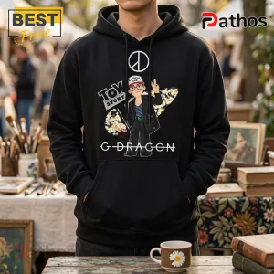 G-Dragon x Toy Story Bullseye Daisy Black Hoodie 2 Black cotton hoodie featuring G-Dragon character graphic, Toy Story logo, daisy floral surfboard, and peace sign symbol.!