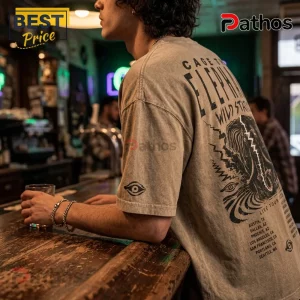 Man wearing tan vintage-wash Cage The Elephant graphic t-shirt with black tour print and eye icon on sleeve in a bar.!