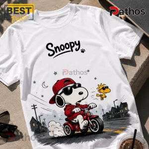 2026 Snoopy We Ride At Dawn Biker T-Shirt 5 White crew neck t-shirt featuring Snoopy in a red hoodie and cap riding a red tricycle with Woodstock wearing sunglasses.!