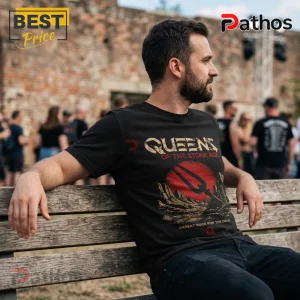 Man wearing black Queens of the Stone Age t-shirt with a red sun, pitchfork, and desert graphic on a blurred park background.!