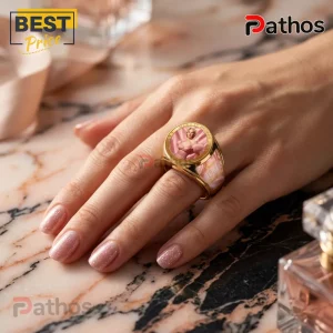 Marilyn Monroe 100th Anniversary gold engraved ring worn on a finger, featuring a pink portrait inlay on marble surface.