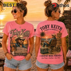 Pink cotton t-shirt featuring Toby Keith graphic prints, cowboy imagery, acoustic guitars, and song titles on a beach sunset.!
